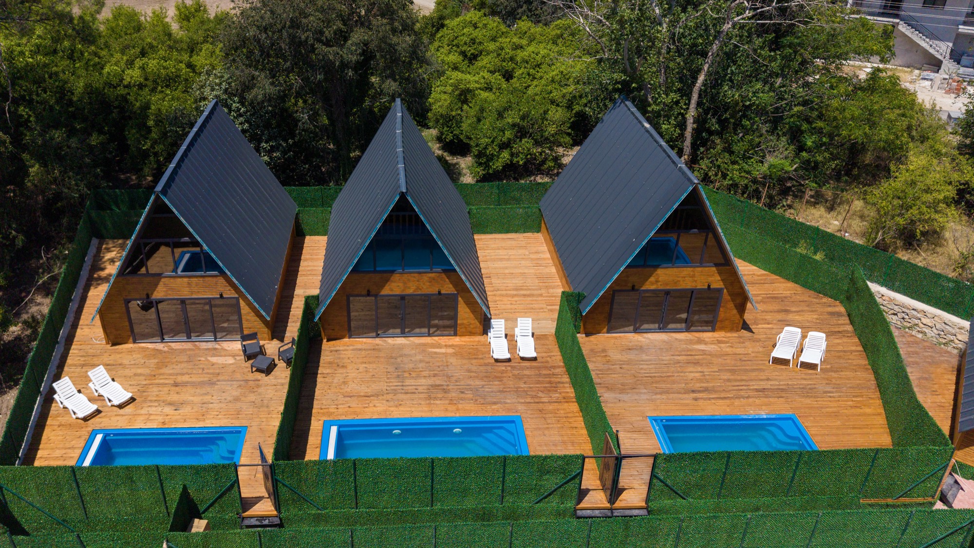 Üç A-frame bungalov; her birinin kendi terası, havuzu ve çiti var